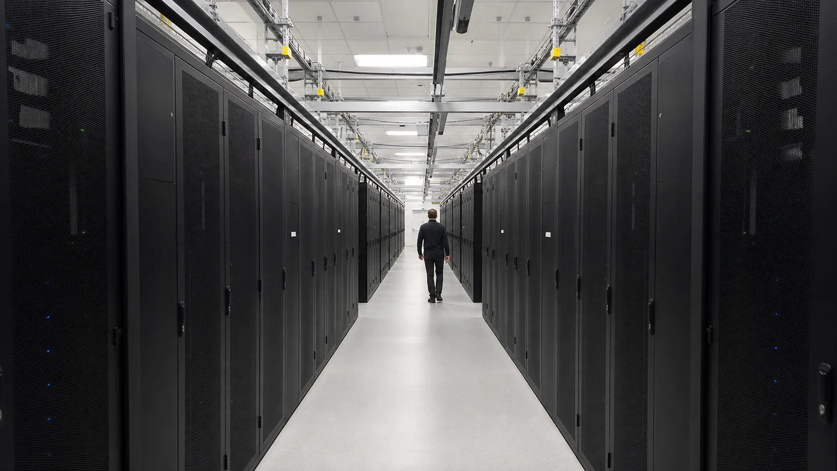 A bright symmetrical compute facility with matte black server cabinets and one engineer for scale.
