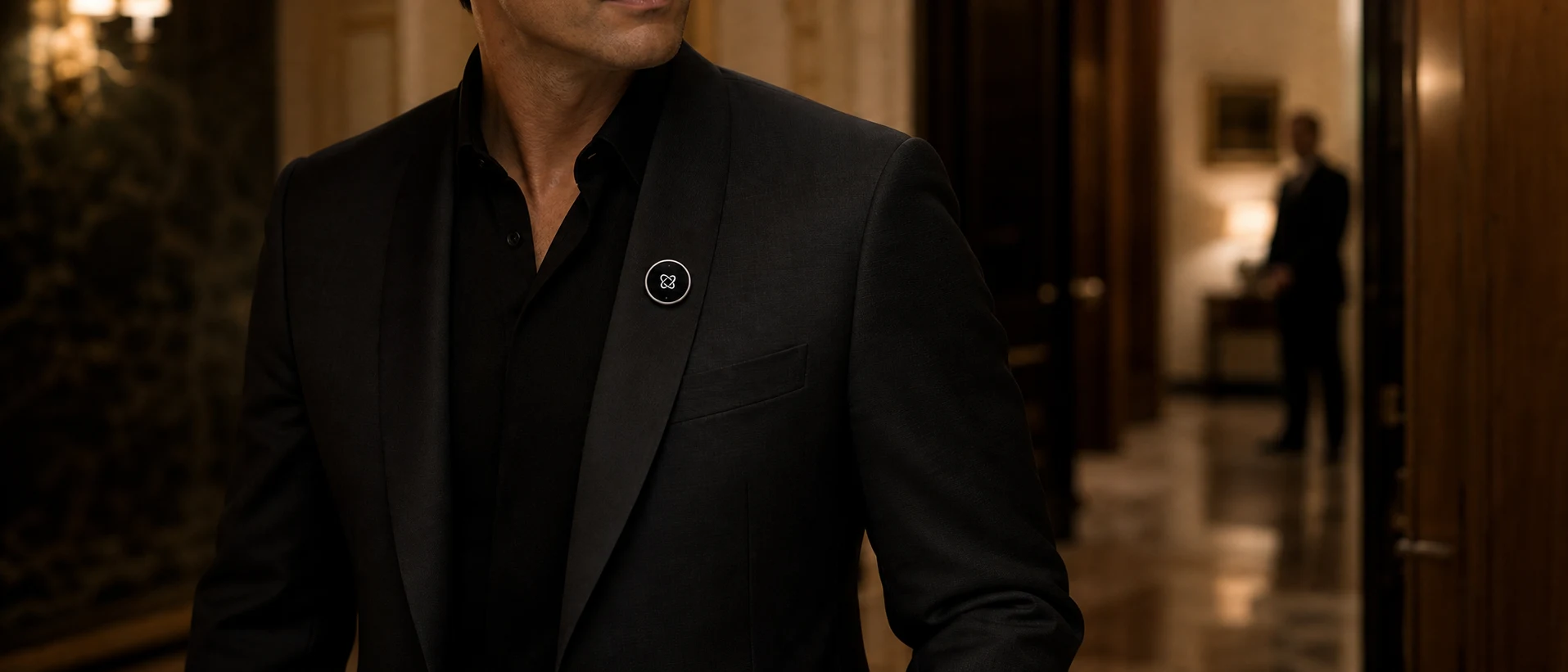 An anonymous principal in a black tailored jacket wearing the circular Attaché Totem between private rooms.